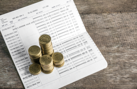 Saving money with gold coin stack and book bank on wood table for investment, business and advertisementの写真素材