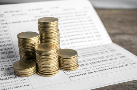 Saving money with gold coin stack and book bank on wood table for investment, business and advertisementの写真素材