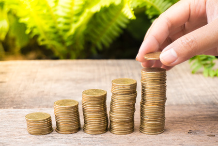 Saving money with gold coins stack and hand on green background for investment, business and advertisementの写真素材