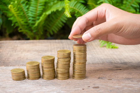 Saving money with gold coins stack and hand on green background for investment, business and advertisementの写真素材