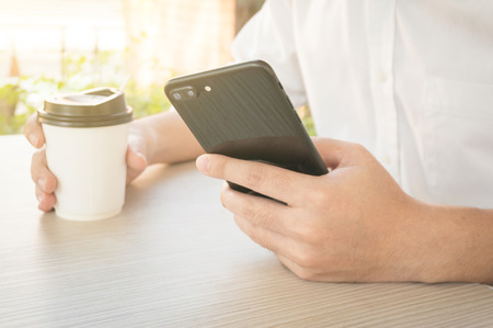 A man is typing phone and holding coffee cup