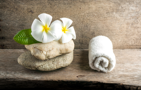 White flower and leafs with big and tiny stone and towel on wood table for health spa advertisement and presentationの写真素材