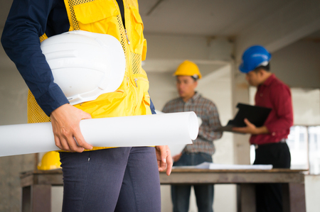 Engineer holding drawing and safety helmet in hand on site backgroundの写真素材