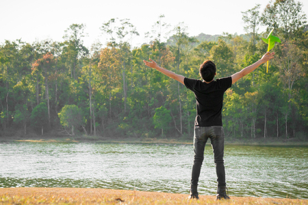 A young man playing a green windmill with freedom feeling on green forest backgroundの写真素材