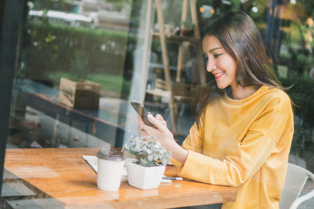 Asian woman chat with friend by mobile phone in cafÃ©の写真素材
