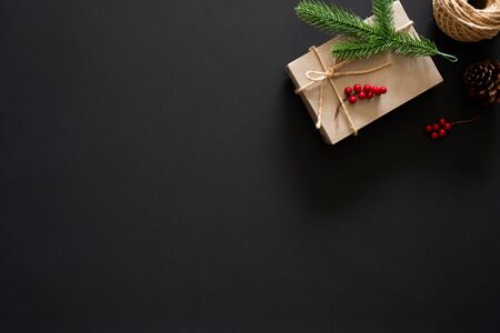 Christmas gift on black background with pine branches, berries and rope. Flat lay, top view, copy spaceの写真素材