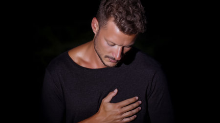 Portrait of a young man suffering from chest pain. Dark background.の素材