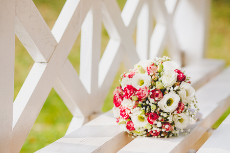 A white pink wedding bouquet of flowers rests on a white benchの写真素材