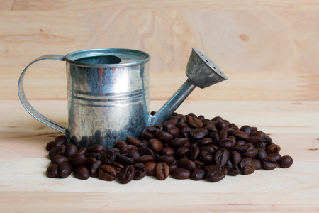 Watering Can miniature and Coffee beans wood background.の写真素材