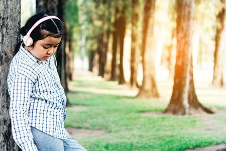 free happy cute girl enjoying. A beautiful kids hipster girl listening to music on headphones in the park.の写真素材