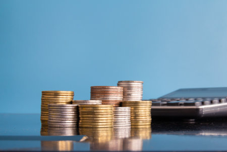 Coins stacked on each other with calculator and blue background, business conceptの写真素材