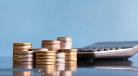 Coins stacked on each other with calculator and blue background, business conceptの写真素材