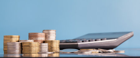 Stacks of coins and calculator on blue background with copy space.の写真素材
