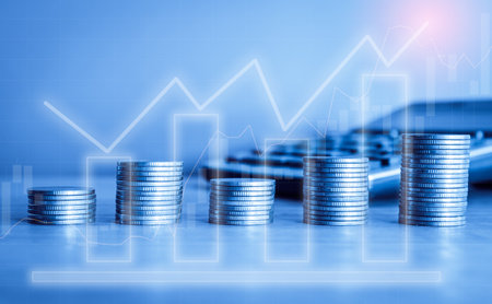 Stacks of coins and calculator with financial graph on blue background.の写真素材