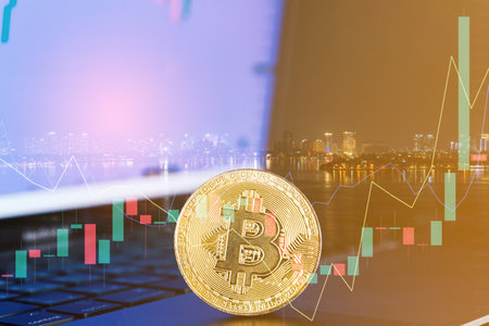 golden bitcoin coin on laptop computer with graph chart and bokeh light backgroundの写真素材
