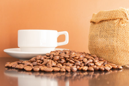 Coffee beans and coffee cup on the table with brown backgroundの写真素材