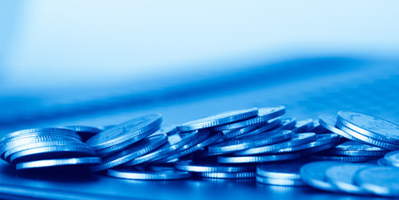 Close-up of stack of coins with laptop computer on blue backgroundの写真素材