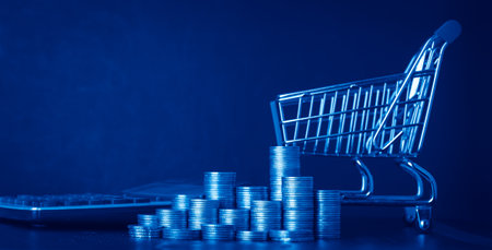 Shopping cart and coins on dark blue background, business and finance concept.の写真素材