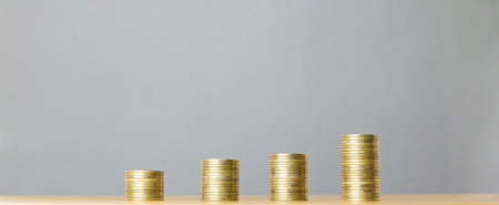 Stacks of gold coins on a wooden table and grey background.の写真素材