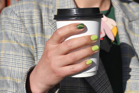 Beautiful female hand with manicure holds cardboard coffee cup. Tender yellow nail polish and green cat eye designの写真素材