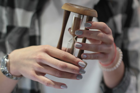 Beautiful female hands with manicure hold an hourglass. Beauty and fashion conceptの写真素材