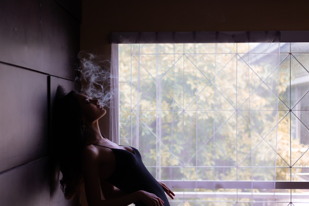 Portrait charming beautiful model woman. Attractive beautiful sexy women is smoking cigarette or weed in dark room at house. Gorgeous woman feels like a dreaming, mind drifting or floating in the airの写真素材