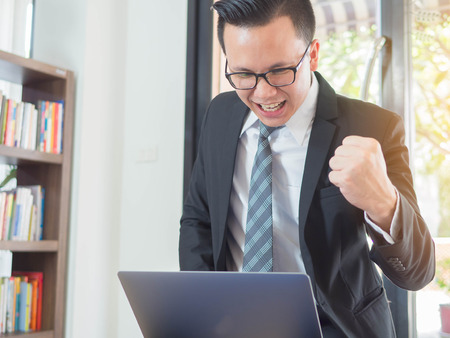 Smiling happy excited businessman using laptop is working in his officeの写真素材
