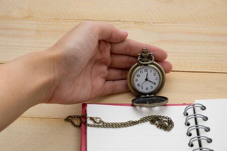 hand fo woman holding pocket watch and empty notebook on wooden backgroundの写真素材