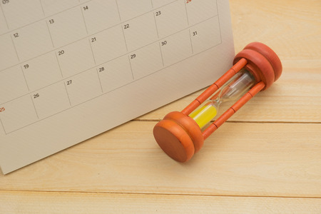 wooden sand clock putting front of calendar on wooden background