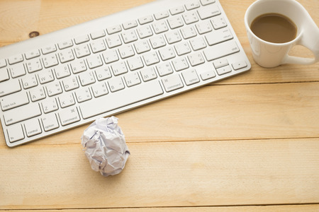 top view. coffee cup with coffee putting on beside keyboard and have worthless paper on wooden background. this image for equipment,business and technology conceptの写真素材