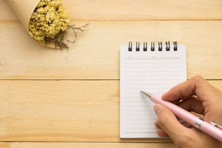 top view. young woman using hand for writing on empty notebook paper and have yellow bouquet flower on top. this image for education,business and body part conceptの写真素材