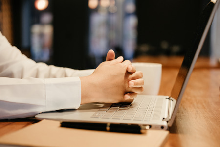 warm tone. business man hold hand placed on laptop. pen and blank notebook placed beside on wooden table. image for computer,person,business,education,body part,place conceptの写真素材