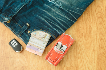 top view. passport book and money insert on pocket blue jean pants with toy car and key placed beside. wooden are background. this image for wear, equipment, accessory, fashion, hobby travel conceptの写真素材