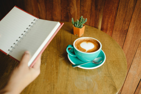 top view. hand of business woman hold blank notebook has cup with coffee and cactus placed on wooden table are background. image for education, business, beverage, object, conceptの写真素材