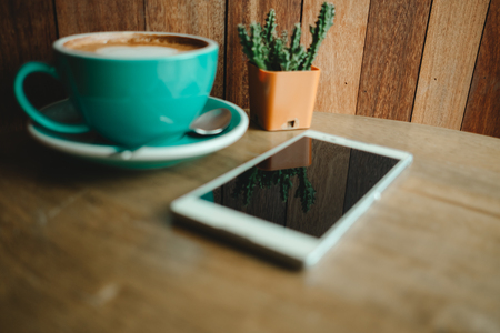 cup with coffee has a heart shape on top and smart phone placed on wooden table. have wooden wall are background. image for business, coffee art, beverage, drink, food, art, technology conceptの写真素材