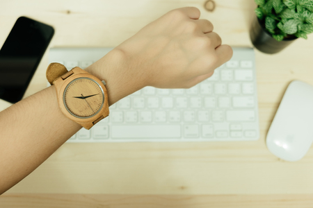 hand of business woman wearing wood watch has smart phone, mouse, plant and keyboard placed on wooden table are background. image for equipment, accessory, fashion, hardware, business conceptの写真素材