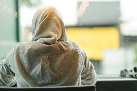 young muslim woman wearing gray shirt sit in a restaurant with window glass are background. this image for people, person, islamic, religion, culture, place conceptの写真素材