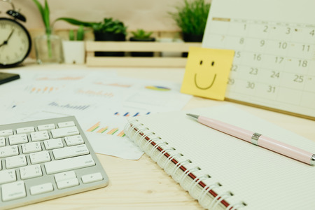 work table with keyboard, pen, blank notebook paper, info graph, clock and has many plants placed are background. image for business, document, education, workplace, marketing, object conceptの写真素材
