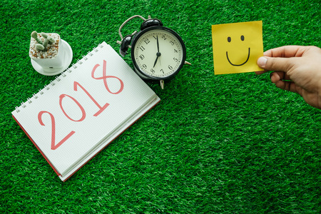 happy new year background with hand hold smile note paper, clock, plants and notebook has message...