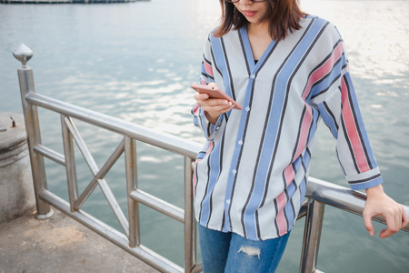 young women stand alone hold mobile phone with sea background. image for nature, travel, person, portrait, tourist, scenery conceptの写真素材
