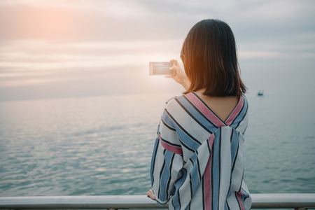 nature background young women stand alone hold mobile phone expression for photography sea. image for travel, person, portrait, tourist, scenery conceptの写真素材