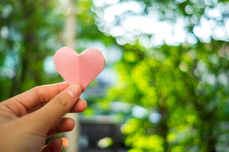 hand of young woman with pink paper heart nature background. image for valentine day, idea, love, celebration, body, copy space, decoration conceptの写真素材