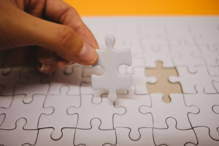 business background hand of businessman pick one piece jigsaw placed on orange table with copy space. image for texture, problem, thinking, idea, toy, puzzle, play, game conceptの写真素材