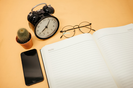 top view business background workspace with glasses, mobile phone, cactus, clock and blank notebook on table. image for education, desktop, copy space, work, smartphone, mock up, communication conceptの写真素材