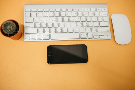top view business table background with cactus, keyboard, mouse, mobile phone place on yellow table. image for copy space, desktop, smartphone, workplaceの写真素材