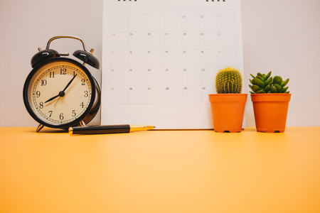 front view. clock, calendar and plant placed on yellow table background with copy space. image for cactus, business, time, object, isolated, modern, decoration, plant, nature, workspace conceptの写真素材