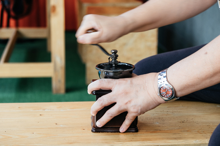 front view. beverage background hand of man mash coffee bean in coffee grinder on wooden table. image for food, raw, cafe, copy space, health, professional, service, equipment conceptの写真素材