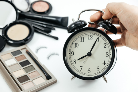 hand of women holding alarm clock and cosmetic object, powder on white table background. image for beauty, business, feminine, time, makeup conceptの写真素材