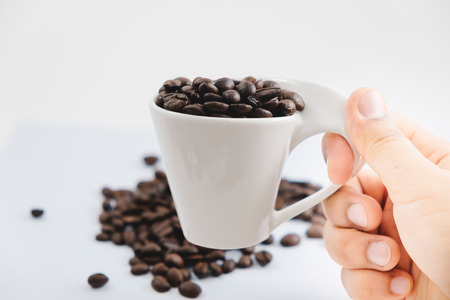 beverage background hand of woman hold cup with coffee bean place on white table with copy space. image for isolated, drink, food, raw, espresso, decoration, plant, cafe conceptの写真素材