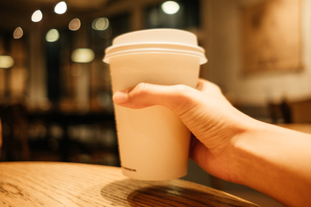food background hand of woman holding coffee glass in restaurant with copy space. image for cafe, beverage, indoor, object, lifestyle conceptの写真素材